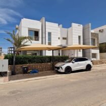 Luxury modern white villas with shaded car park and green landscaping under a bright blue sky, ideal property.