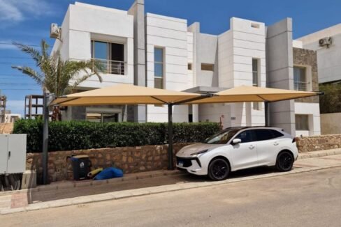 Luxury modern white villas with shaded car park and green landscaping under a bright blue sky, ideal property.