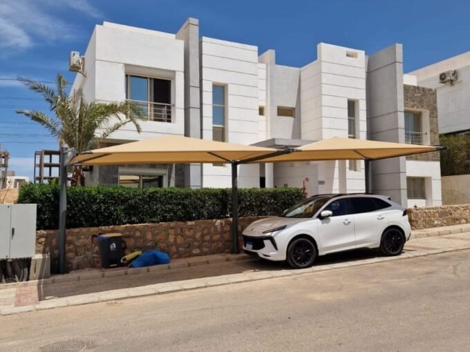 Luxury modern white villas with shaded car park and green landscaping under a bright blue sky, ideal property.