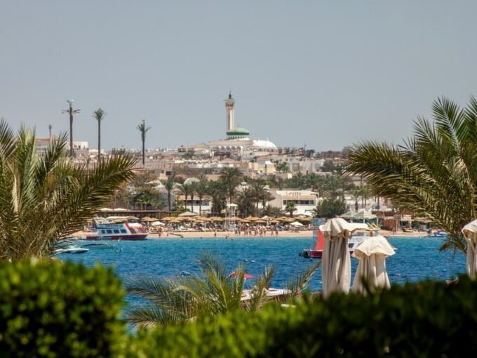 Beach view with Hurghada skyline and lighthouse in the background.